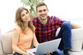 Young couple of students uses a laptop sitting on sofa Royalty Free Stock Photo