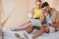 young couple in sunglasses using laptop while sitting Royalty Free Stock Photo