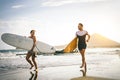 Young couple of surfers running with surfboards on the beach at sunset - Happy lovers going to surf together Royalty Free Stock Photo