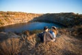 Young couple in sweater and hat sitting near autumn lake smiling having good time