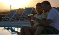 Young couple takes an aperitif drinking a glass of red wine at sunset exchanging cuddles