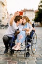 Young Couple taking Selfie. Pretty happy young disabled woman in wheelchair kissing with her young boyfriend and smiling Royalty Free Stock Photo