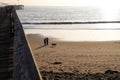 A young couple with their dog walking along the silky brown sands of the beach at sunset near a long brown wooden pier Royalty Free Stock Photo