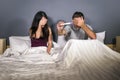 Young couple together in bed nervous and stressed covering eyes for not seeing pregnancy test holding predictor feeling panic emot Royalty Free Stock Photo