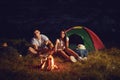 Young couple tourists on camping night cook bread by campfire