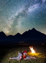 Young couple tourists lying near the campfire under incredibly beautiful starry sky and Milky way at night. Low light Royalty Free Stock Photo