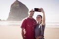 A young couple of tourists make selfies in front of the Haystack Rock in Cannon Beach, Oregon, USA. Royalty Free Stock Photo