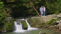 A young couple of tourists are standing near a waterfall on a mountain river. Admire the beautiful scenery. Tourism and