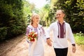 A young couple in a traditional Ukrainian clothing whith bouquet walking in the sunny park