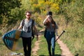 Young couple of travelers with backpack, guitar and sup board going through green countryside road