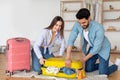 Young couple trying to close full of clothes suitcase, preparing for vacation and packing things together at home