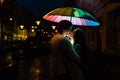 Young couple under an umbrella kisses at night on a city street.