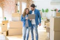 Young couple using computer laptop standing on a room around cardboard boxes, happy for moving to a new apartment Royalty Free Stock Photo