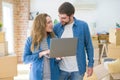 Young couple using computer laptop standing on a room around cardboard boxes, happy for moving to a new apartment Royalty Free Stock Photo