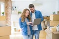 Young couple using computer laptop standing on a room around cardboard boxes, happy for moving to a new apartment Royalty Free Stock Photo
