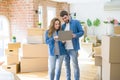 Young couple using computer laptop standing on a room around cardboard boxes, happy for moving to a new apartment Royalty Free Stock Photo