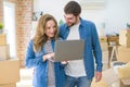 Young couple using computer laptop standing on a room around cardboard boxes, happy for moving to a new apartment Royalty Free Stock Photo