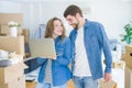 Young couple using computer laptop standing on a room around cardboard boxes, happy for moving to a new apartment Royalty Free Stock Photo