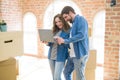 Young couple using computer laptop standing on a room around cardboard boxes, happy for moving to a new apartment Royalty Free Stock Photo