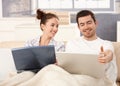 Young couple using laptop in bed at home smiling Royalty Free Stock Photo