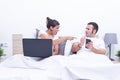 Young couple using laptop and mobile phone in bed at home. .she recriminates something he is seeing on the cell phone. Intermet Royalty Free Stock Photo