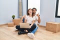 Young couple using laptop at new home doing happy thumbs up gesture with hand Royalty Free Stock Photo