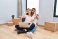 Young couple using laptop at new home doing ok gesture with hand smiling, eye looking through fingers with happy face Royalty Free Stock Photo