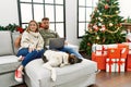 Young couple using laptop sitting by christmas tree smiling looking to the side and staring away thinking Royalty Free Stock Photo