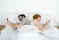 Young couple using mobile phone in bed ignoring each other in relationship communication problems Royalty Free Stock Photo