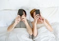 Young couple using mobile phone in bed ignoring each other in relationship communication problems Royalty Free Stock Photo
