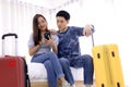 Young couple using mobile phone while sitting together on bed at a hotel room with a suitcase. Royalty Free Stock Photo