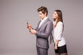 Young couple is using smart phones and smiling while standing back to back on a gray background. Woman look at man. Royalty Free Stock Photo