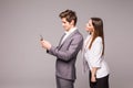 Young couple is using smart phones and smiling while standing back to back on a gray background. Woman look at man. Royalty Free Stock Photo