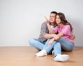 Young couple visualizing the decor of their new home sitting on the bare wooden floor pointing out and discussing placement of fur Royalty Free Stock Photo