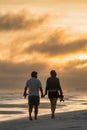 Young couple walking along a sandy beach with the beautiful sunset in the background Royalty Free Stock Photo