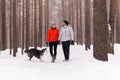 Young couple walking a dog in the winter forest, the dog wants to play Royalty Free Stock Photo