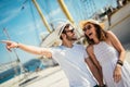 Young couple walking by the harbor of a touristic sea resort with sailboats on background