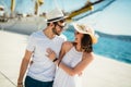 Young couple walking by the harbor of a touristic sea resort with sailboats on background