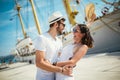 Young couple walking by the harbor of a touristic sea resort with sailboats on background