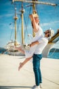 Young couple walking by the harbor of a touristic sea resort with sailboats on background