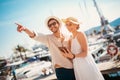 Young couple walking by the harbor using digital tablet of a touristic sea resort with sailboats on background