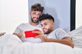Young couple watching video on smartphone sitting on bed at bedrooom