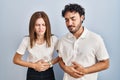 Young couple wearing casual clothes standing together with hand on stomach because indigestion, painful illness feeling unwell Royalty Free Stock Photo