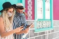 Young couple wearing face protective mask while using mobile phone and holding travel map - Travelers people enjoying first trip