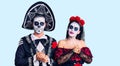 Young couple wearing mexican day of the dead costume over background with hands together and crossed fingers smiling relaxed and