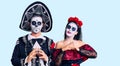 Young couple wearing mexican day of the dead costume over background hands together and fingers crossed smiling relaxed and