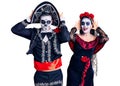 Young couple wearing mexican day of the dead costume over background smiling cheerful playing peek a boo with hands showing face