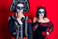 Young couple wearing mexican day of the dead costume over red looking stressed and nervous with hands on mouth biting nails