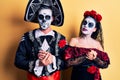 Young couple wearing mexican day of the dead costume over yellow with hands together and crossed fingers smiling relaxed and