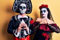 Young couple wearing mexican day of the dead costume over yellow hands together and fingers crossed smiling relaxed and cheerful